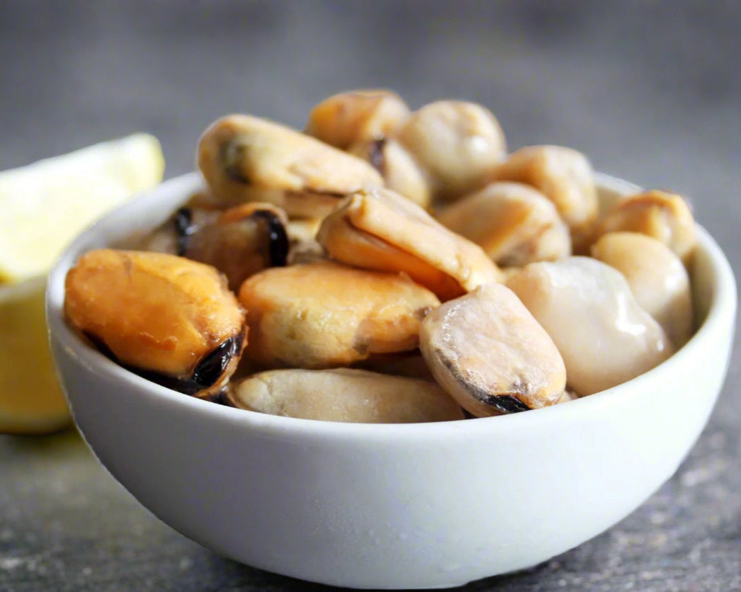 Mussels in a white bowl with lemon wedges on a gray surface